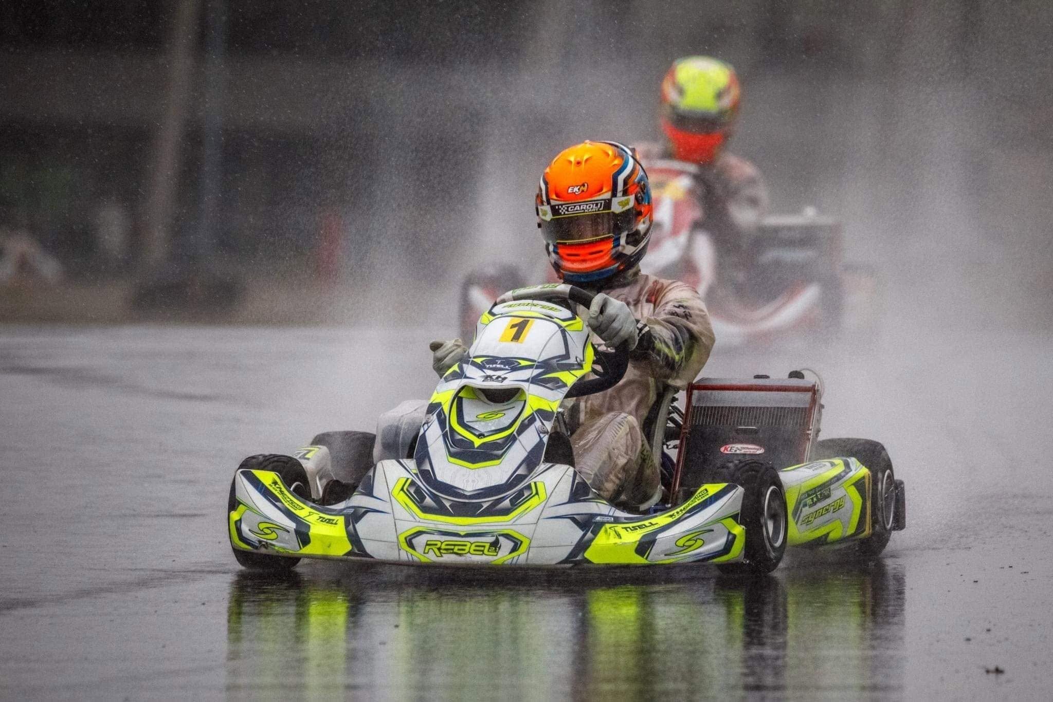 Synergy kart number 1 drives through spray on a rain-soaked track, another kart blurred behind