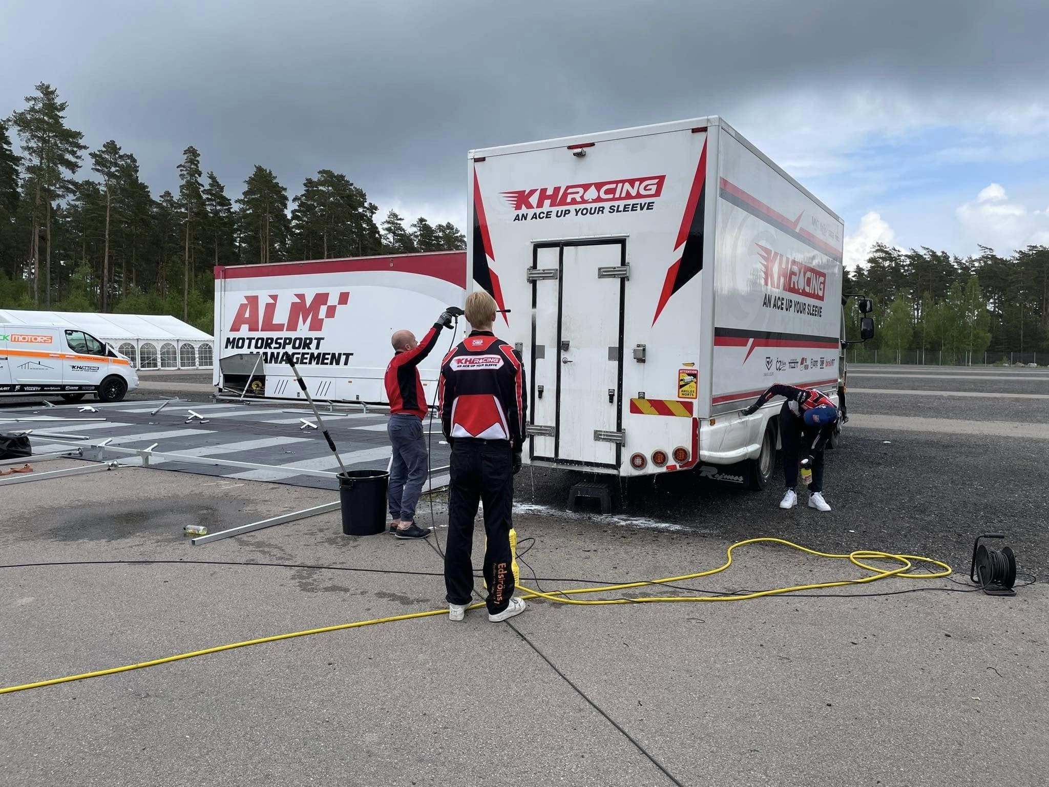 Team members wash the KH Racing truck, with its logo and "An ace up your sleeve", in the paddock