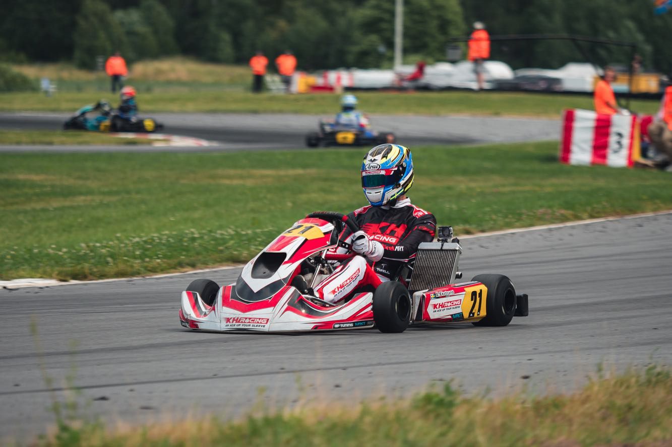Driver in KH Racing’s red and white kart number 21 powering out of a corner